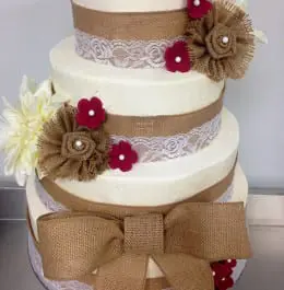 A white wedding cake with a burlap ribbon wrapped around it