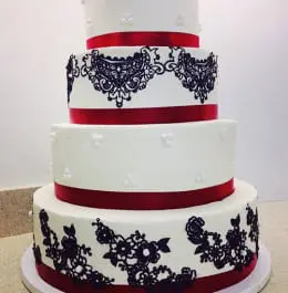 A white wedding cake adorned with roses made of black lace