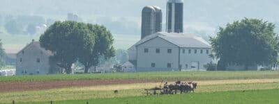 Amish man plowing a field witha team of horses and farm equipment in a field demonstrating the hard working ethic of Amish culture.